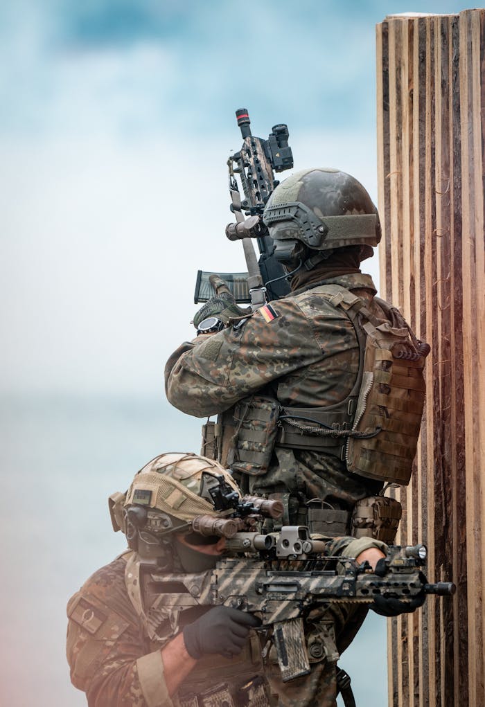 Two soldiers in camouflage uniforms with rifles in action during a military exercise.